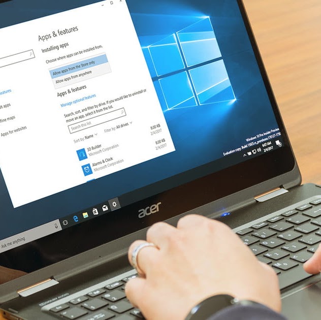 Two human hands belonging to the same person, typing on a laptop computer running Microsoft Windows. The Apps and Features window is open on the computer.